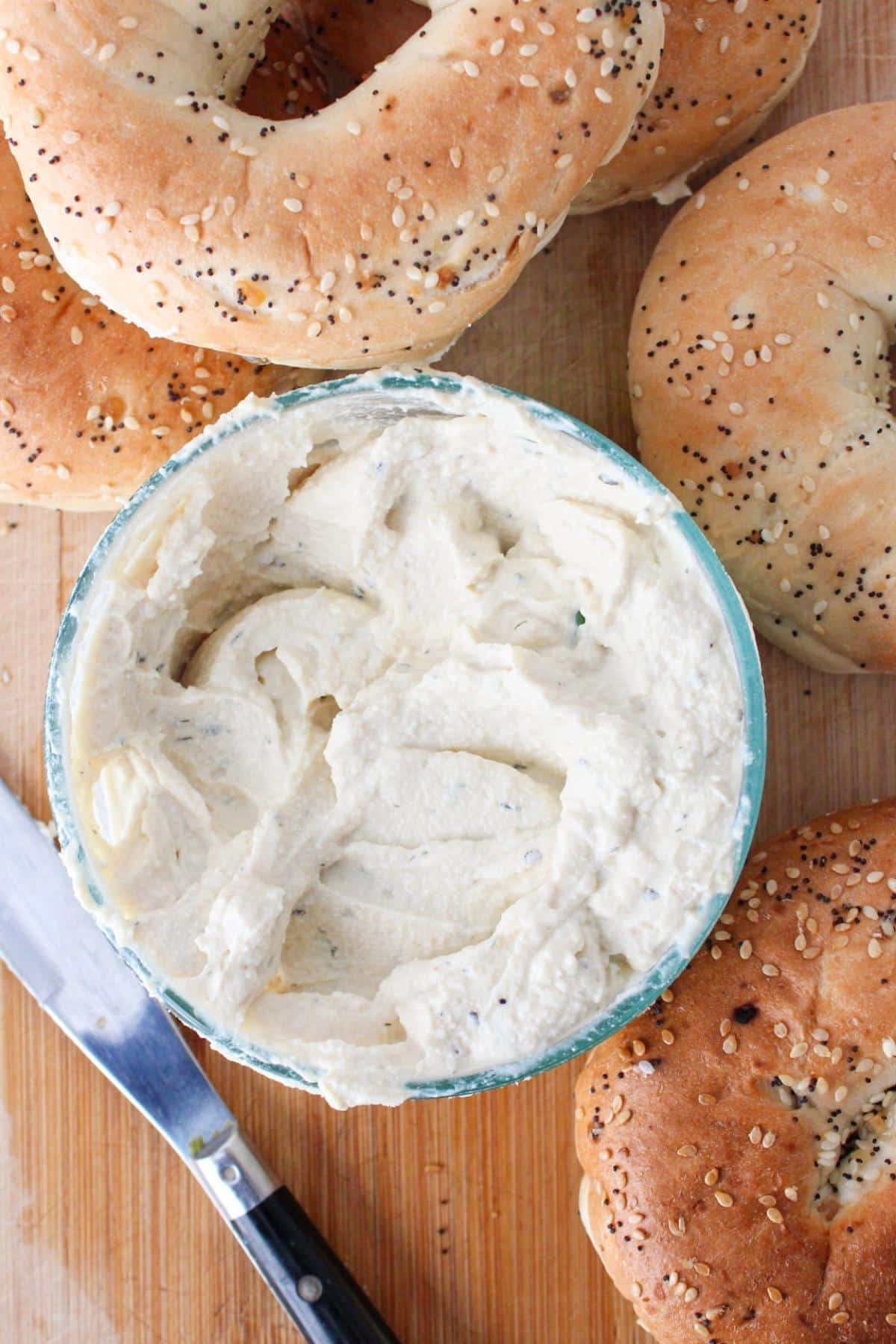A small bowl of tofu cream cheese on a cutting board with bagels.