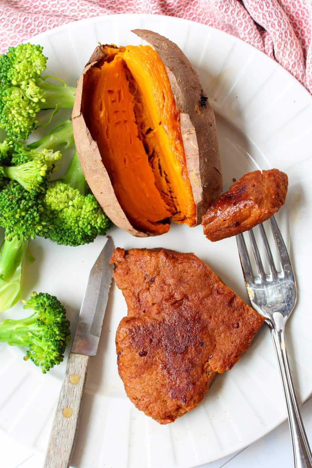 Piece of vegan steak on a plate with broccoli and a baked sweet potato.