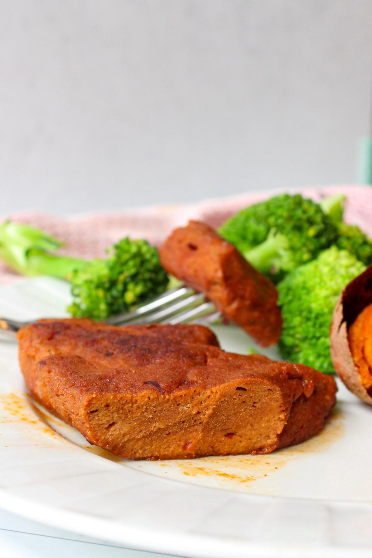 Piece of vegan steak on a plate with broccoli and a baked sweet potato.