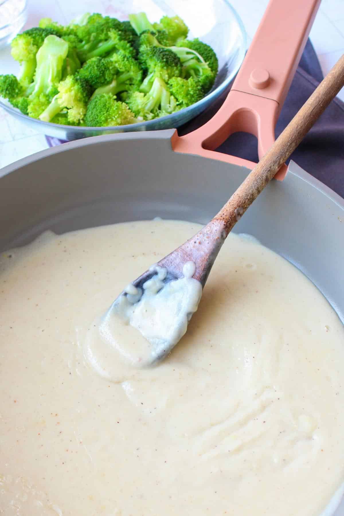Vegan bechamel sauce in a pan next to a bowl of steamed broccoli