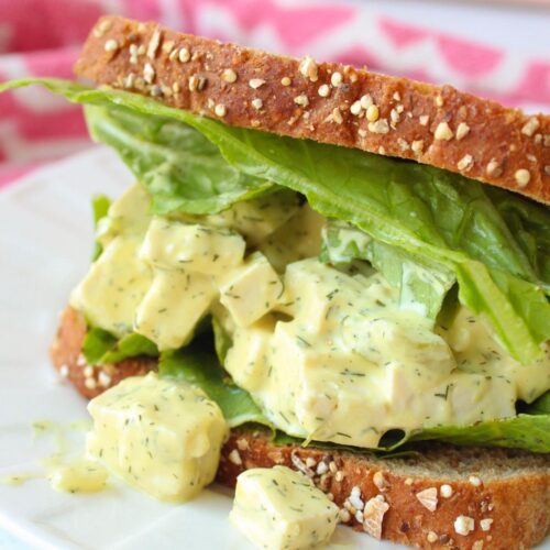 Close up of a vegan egg salad sandwich made with tofu on a plate with lettuce.