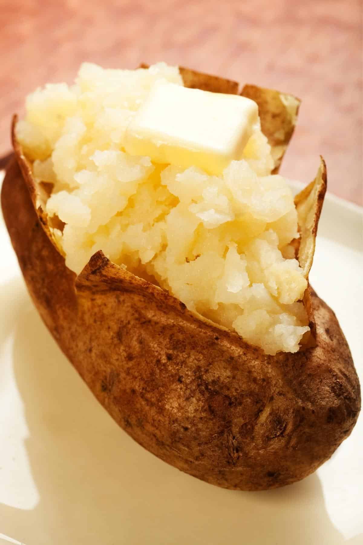 Baked potato without foil on a plate topped with butter.