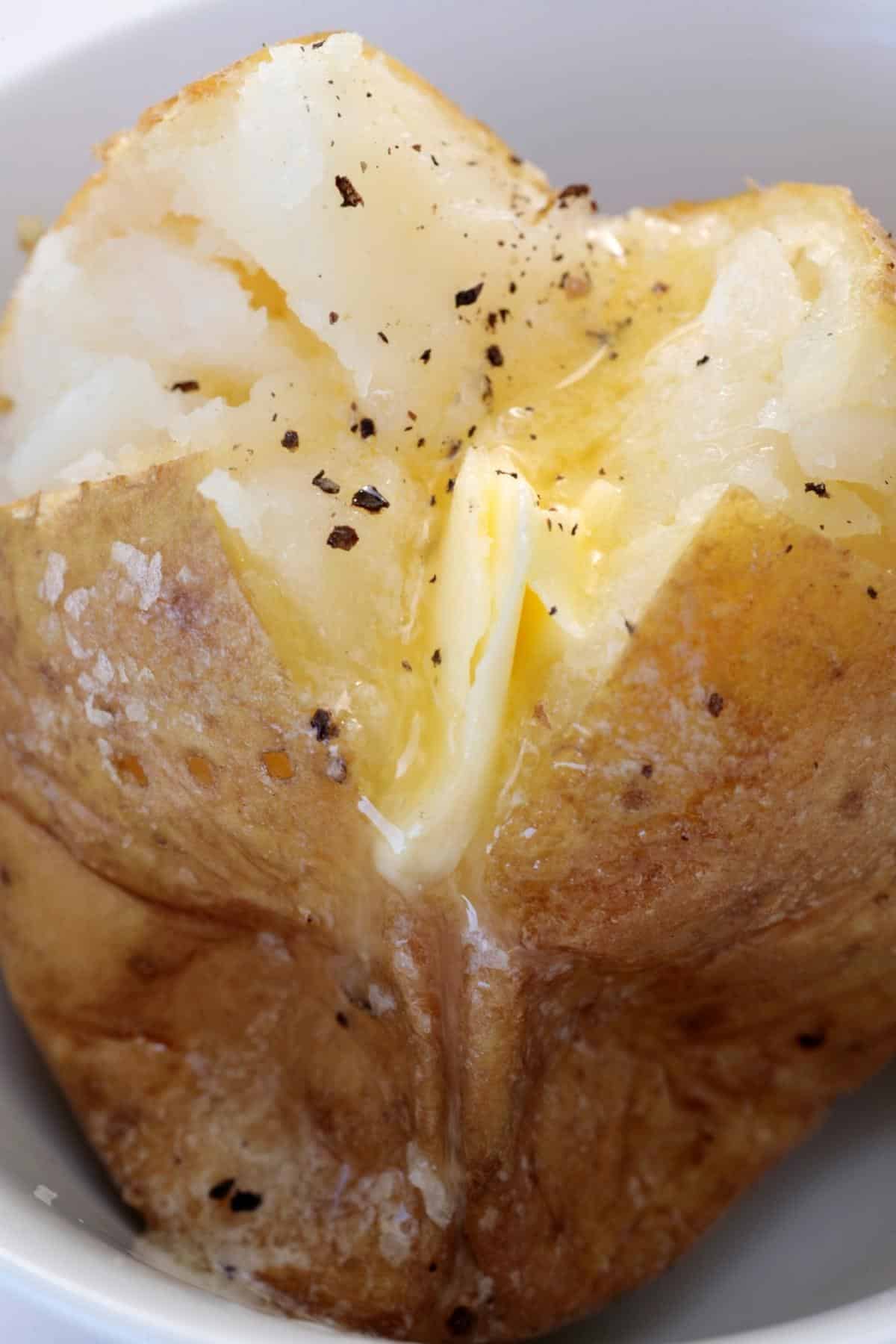 Baked potato without foil on a plate topped with butter.