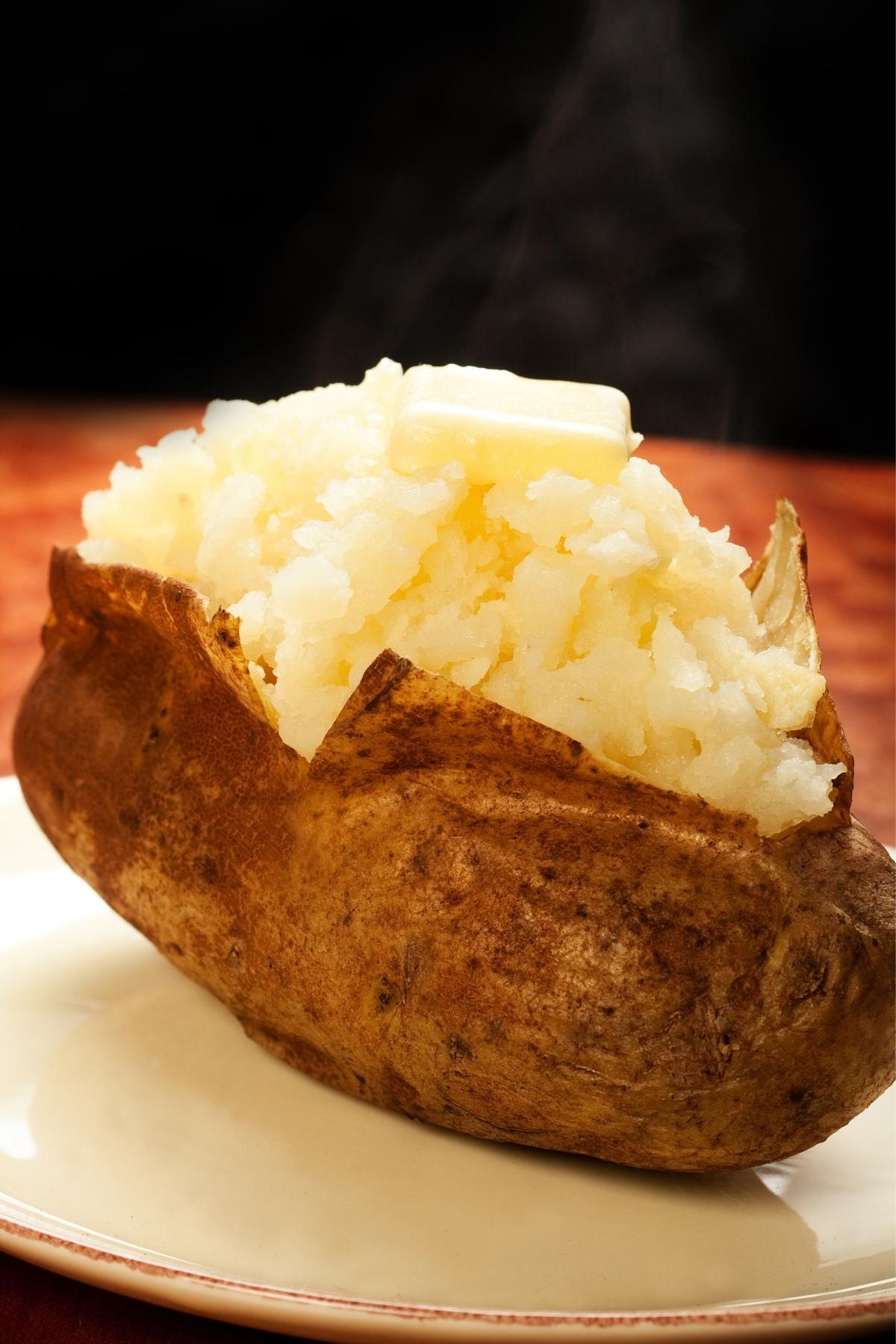Baked potato without foil on a plate topped with butter.
