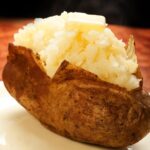 Baked potato without foil on a plate topped with butter.