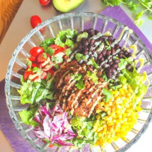 Easy vegan taco salad in a large glass serving bowl topped with beans, corn and tomatoes