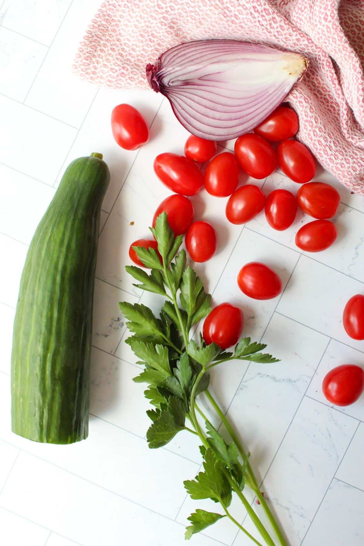 English cucumber, parsley, red onion and tomatoes on a counter top.