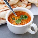 Cup of cooked red lentils with naan bread in the background