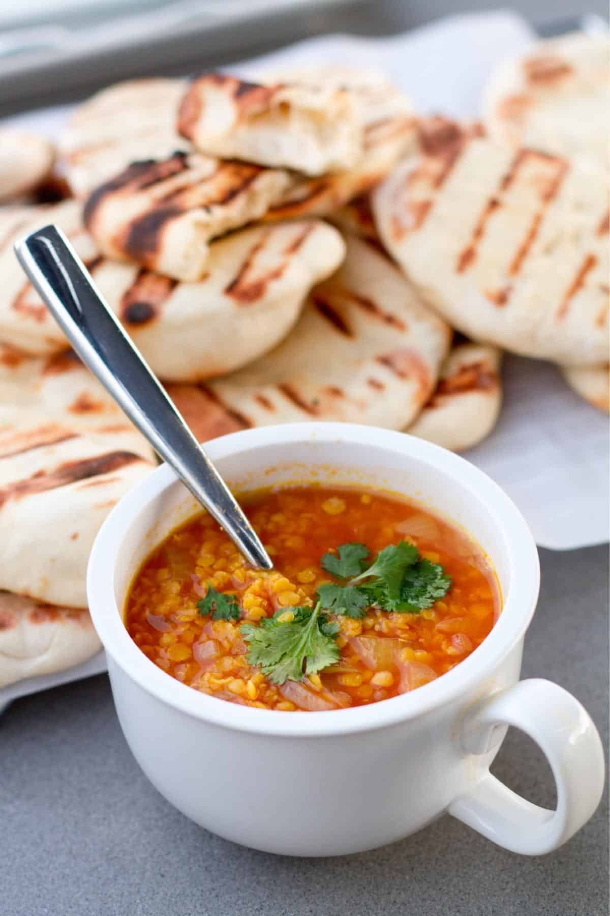 Cup of cooked red lentils with naan bread in the background