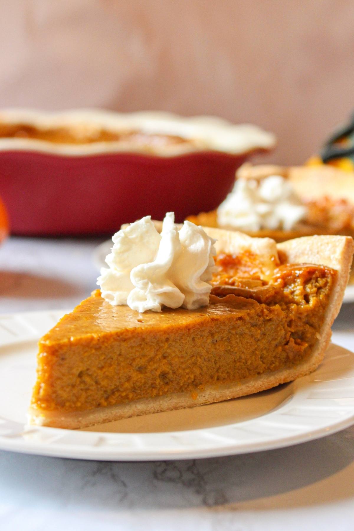 Eggless pumpkin pie slice on a dish topped with whipped cream.