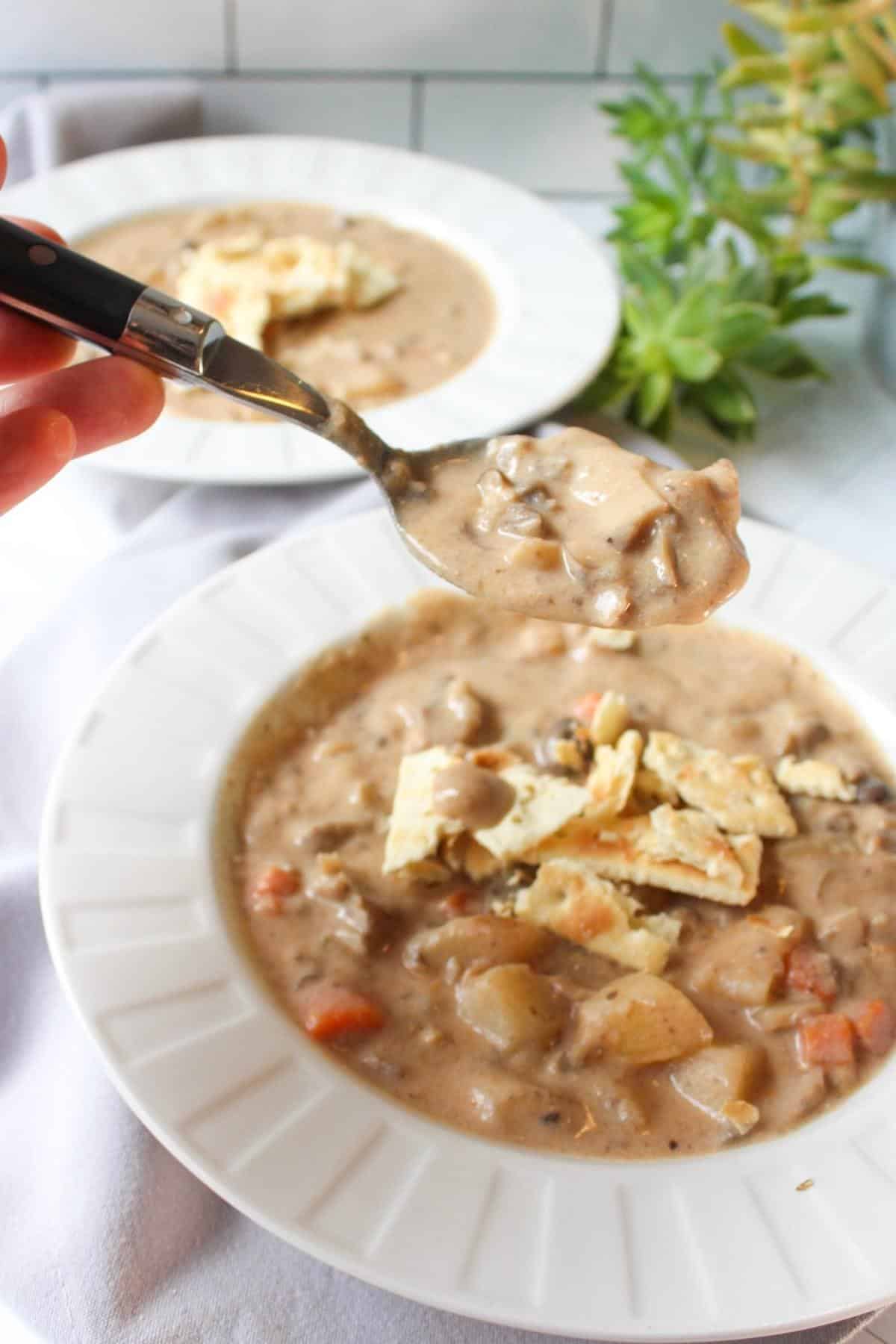 Vegan clam chowder in a bowl with a hand holding a spoonful above it.