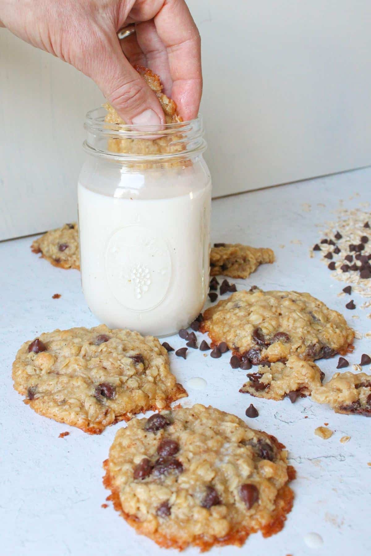 Hand dunking a piece of vegan oatmeal chocolate chip cookie into a glass of soy milk.