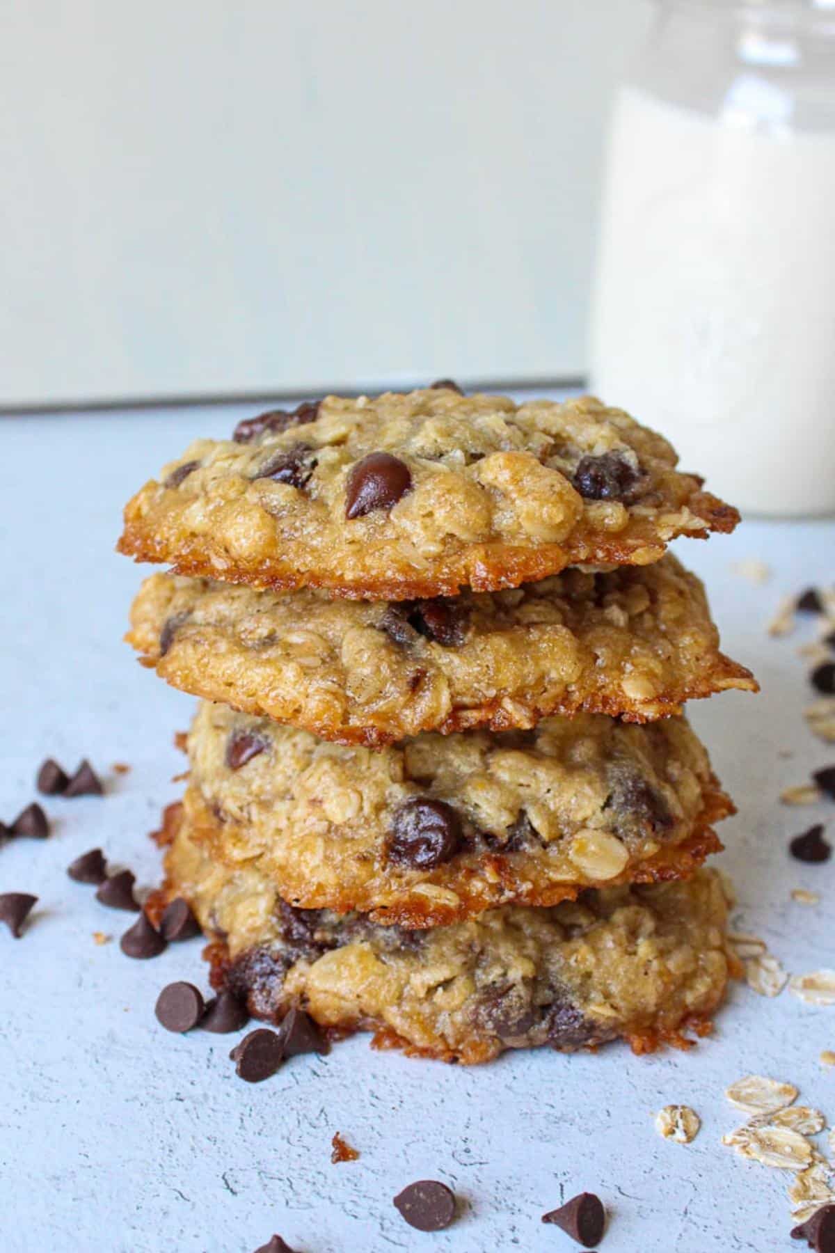 Vegan oatmeal chocolate chip cookies stacked on top of each other with soy milk in the background.