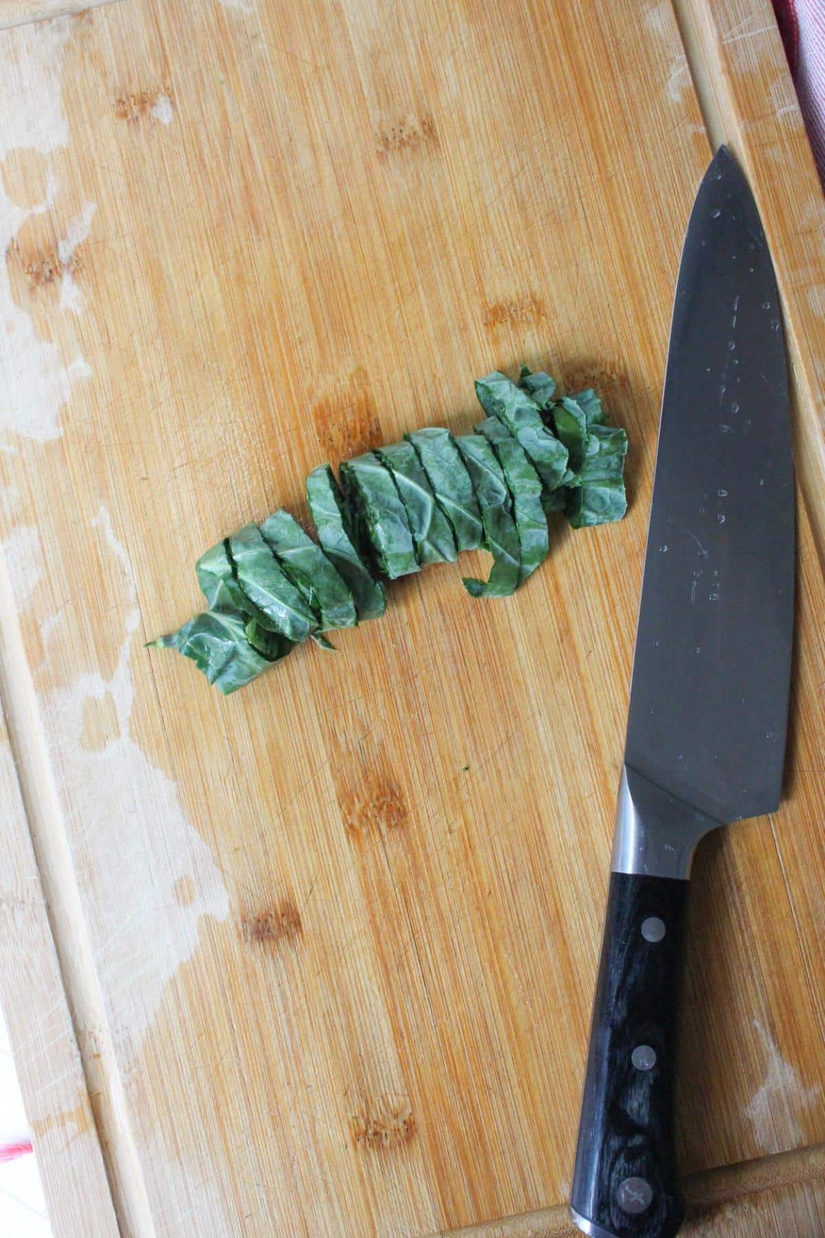 Collard green leaf being cut up on a cutting board.