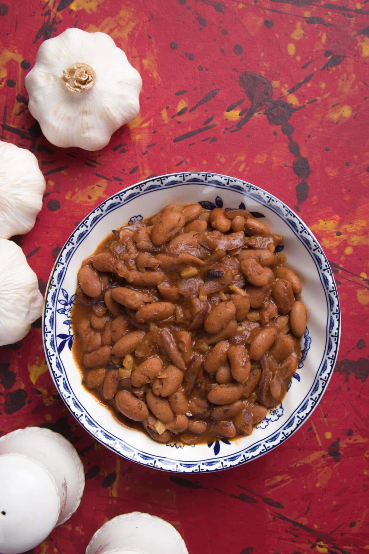 A bowl of cooked pinto beans next to a few bulbs of garlic.