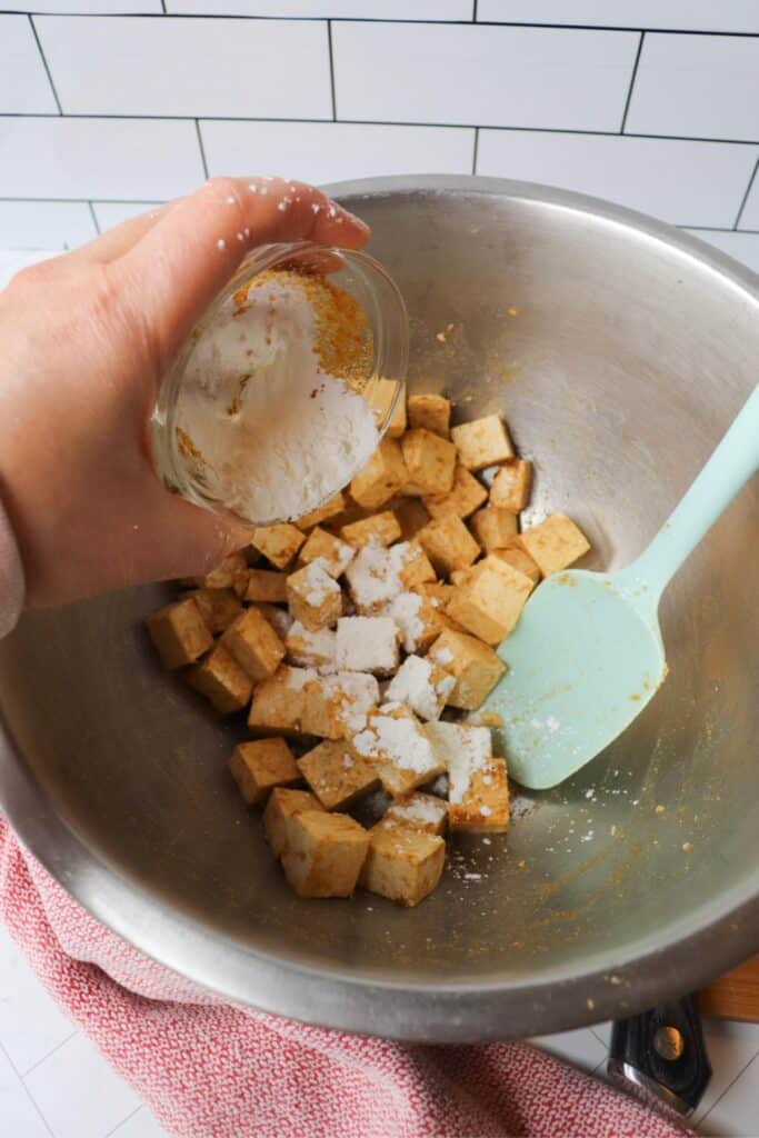 Tofu cubes in a mixing bowl with corn starch getting sprinkled on them.