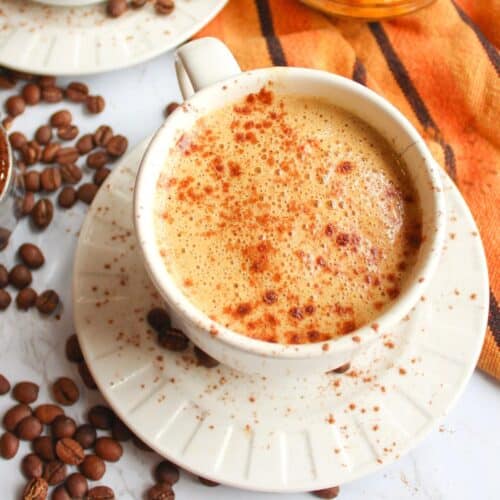 Mug of vegan pumpkin spice latte on a table with coffee beans
