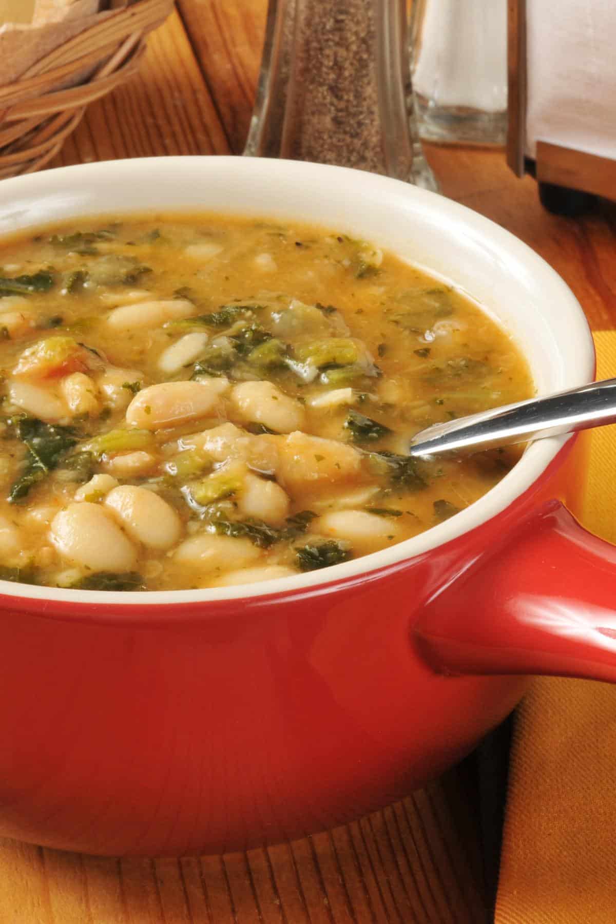 Large red mug of white bean soup with a spoon.