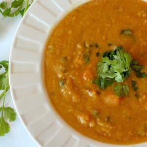 Curry red lentil soup served in a white bowl topped with cilantro.