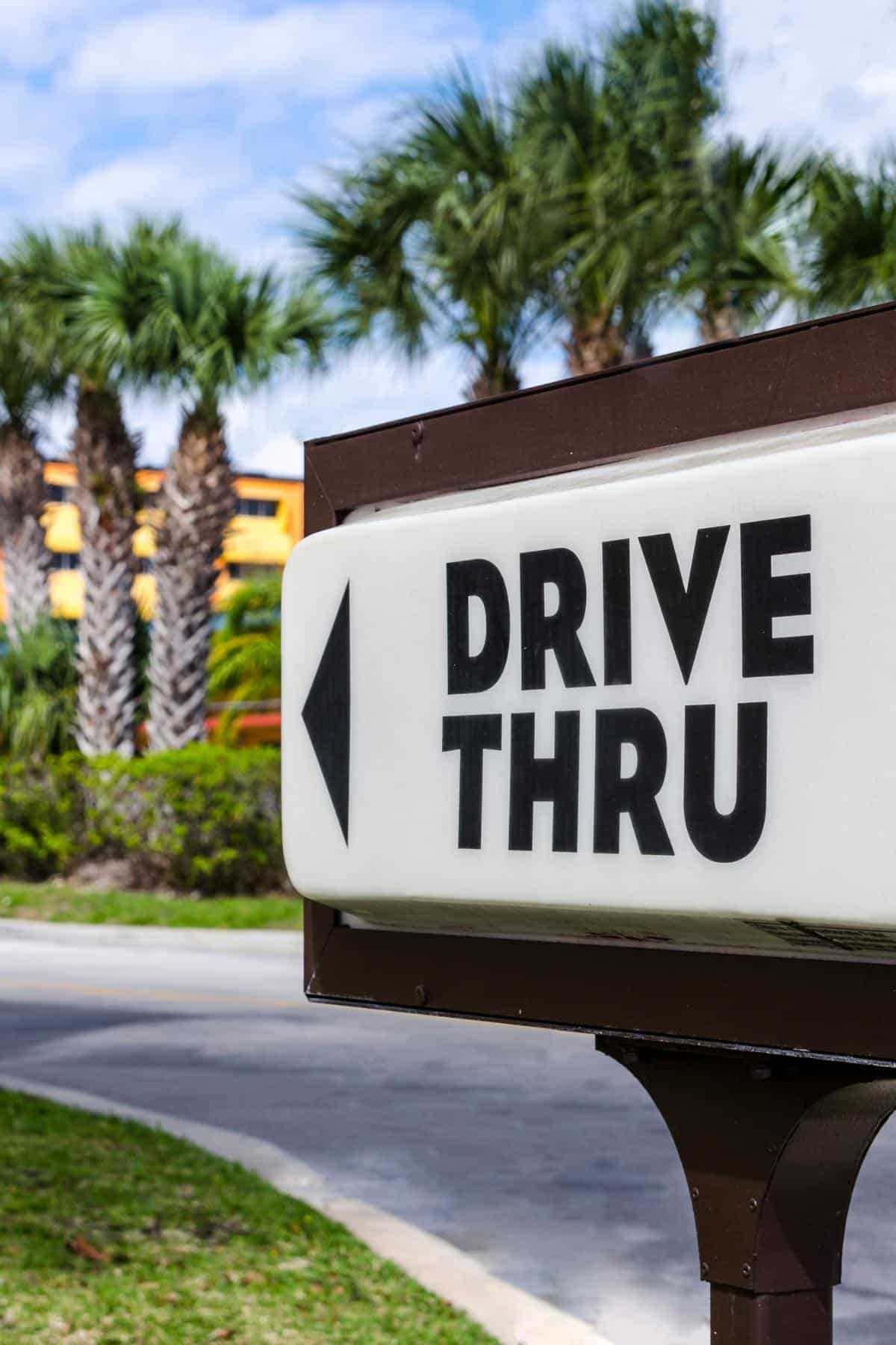 A drive through sign with palm trees behind it.
