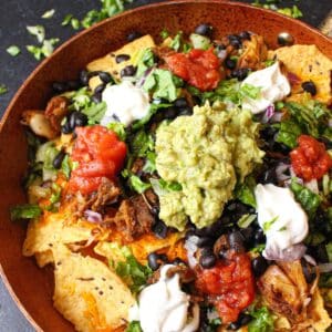 Jackfruit nachos in a large pan topped with guacamole, lettuce, salsa and vegan sour cream.