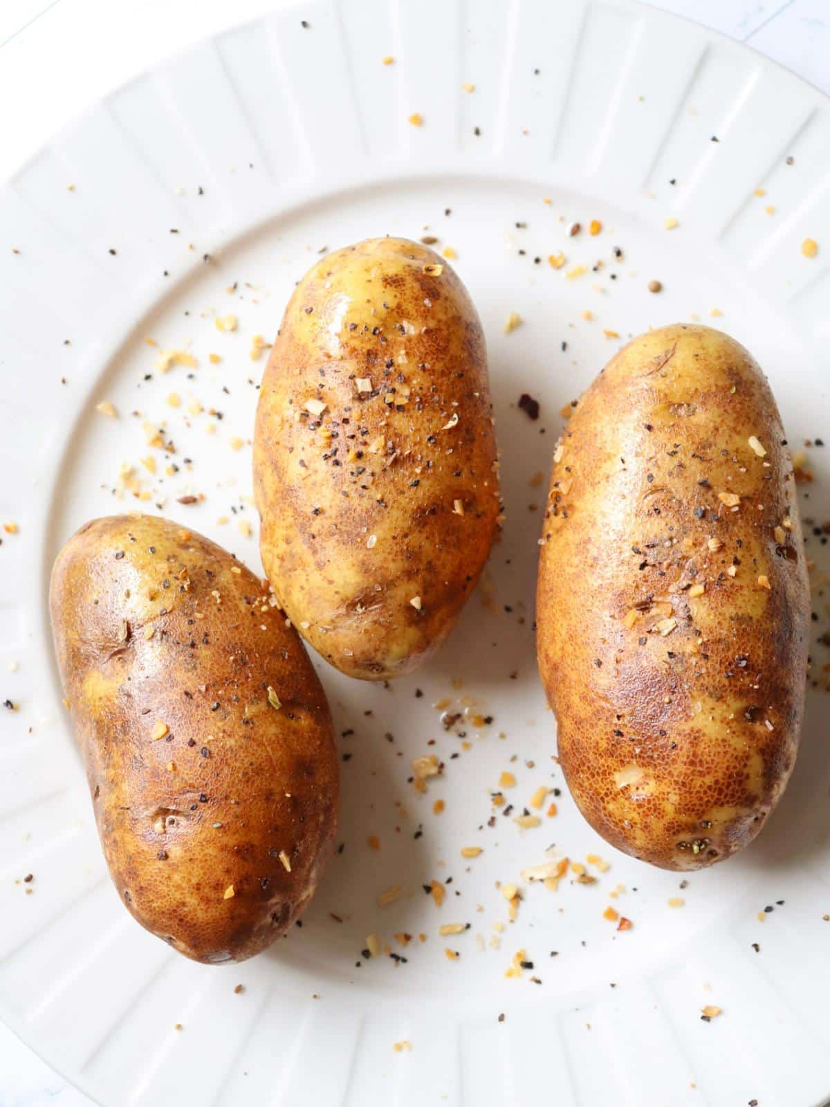 Three potatoes brushed with oil and topped with seasonings.