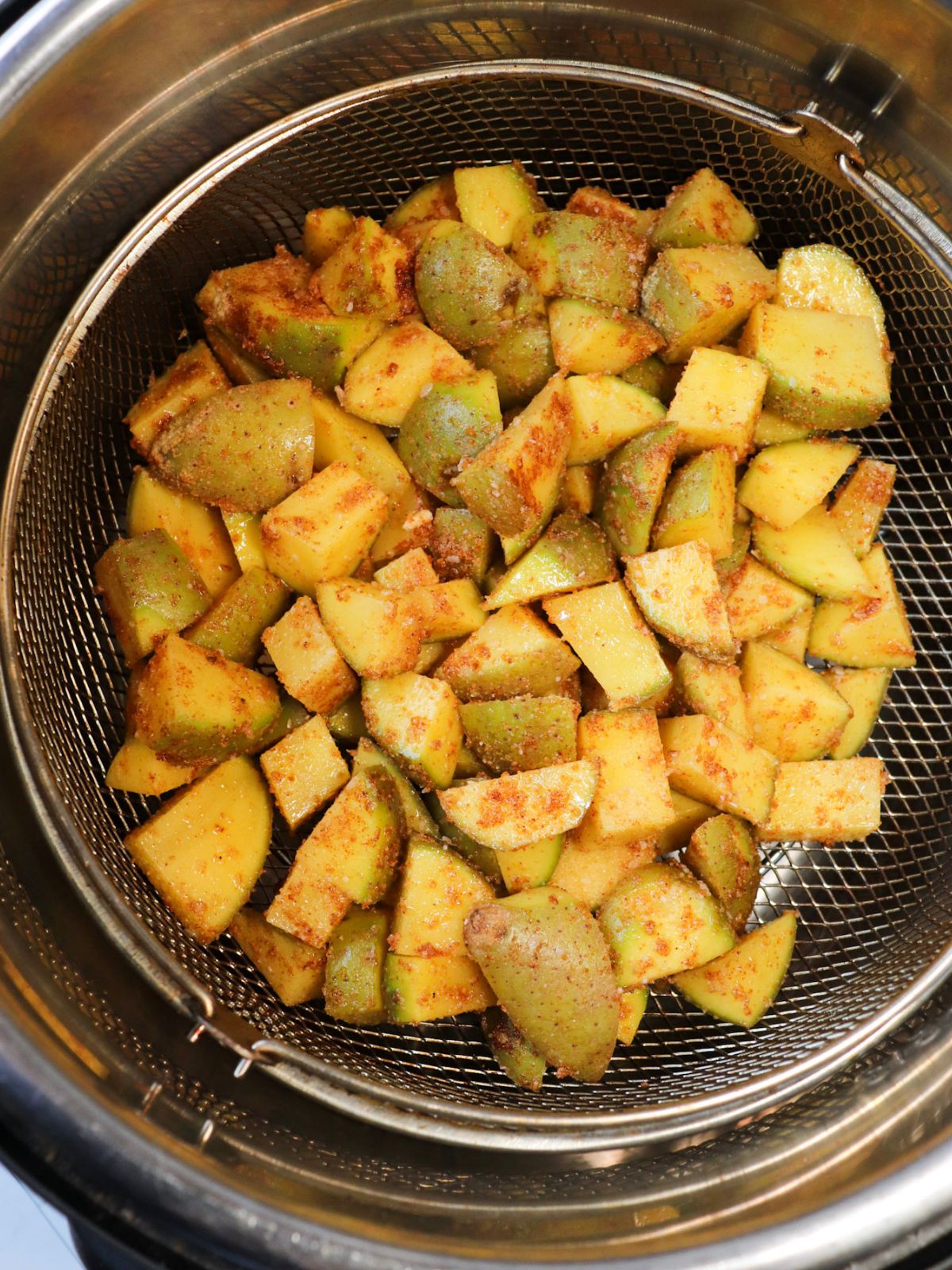 Oiled and seasoned diced potatoes in an air fryer basket before being air fried.