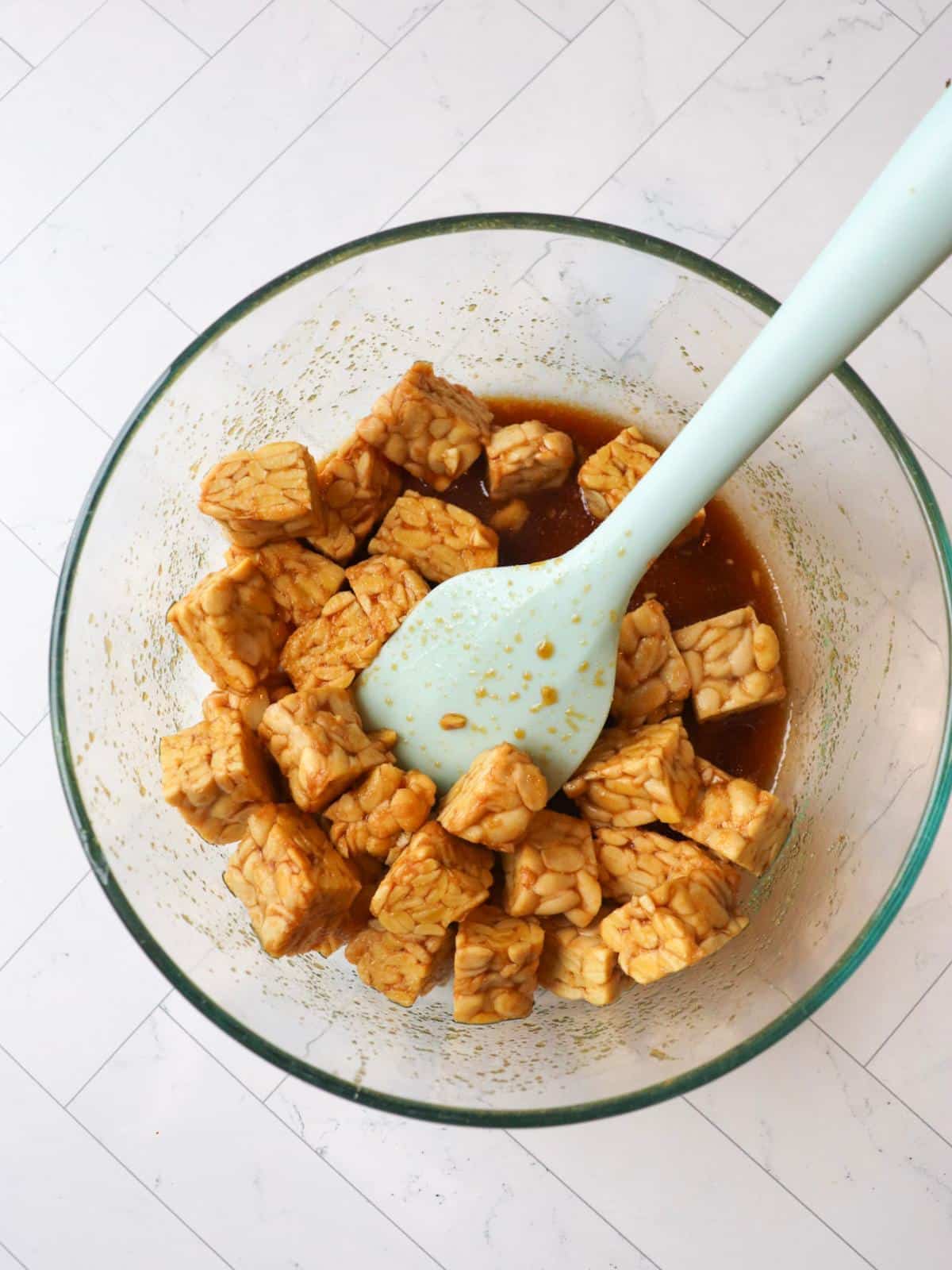 Tempeh cubes marinating in a sauce in a glass bowl.