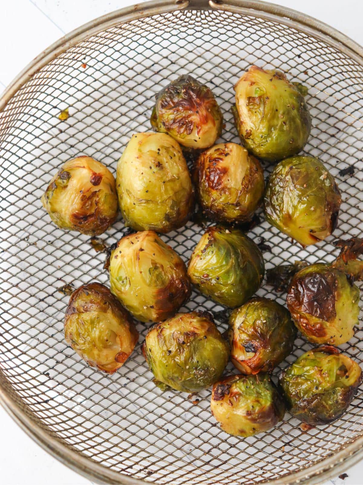 Frozen brussels sprouts in an air fryer basket, after being air fried.