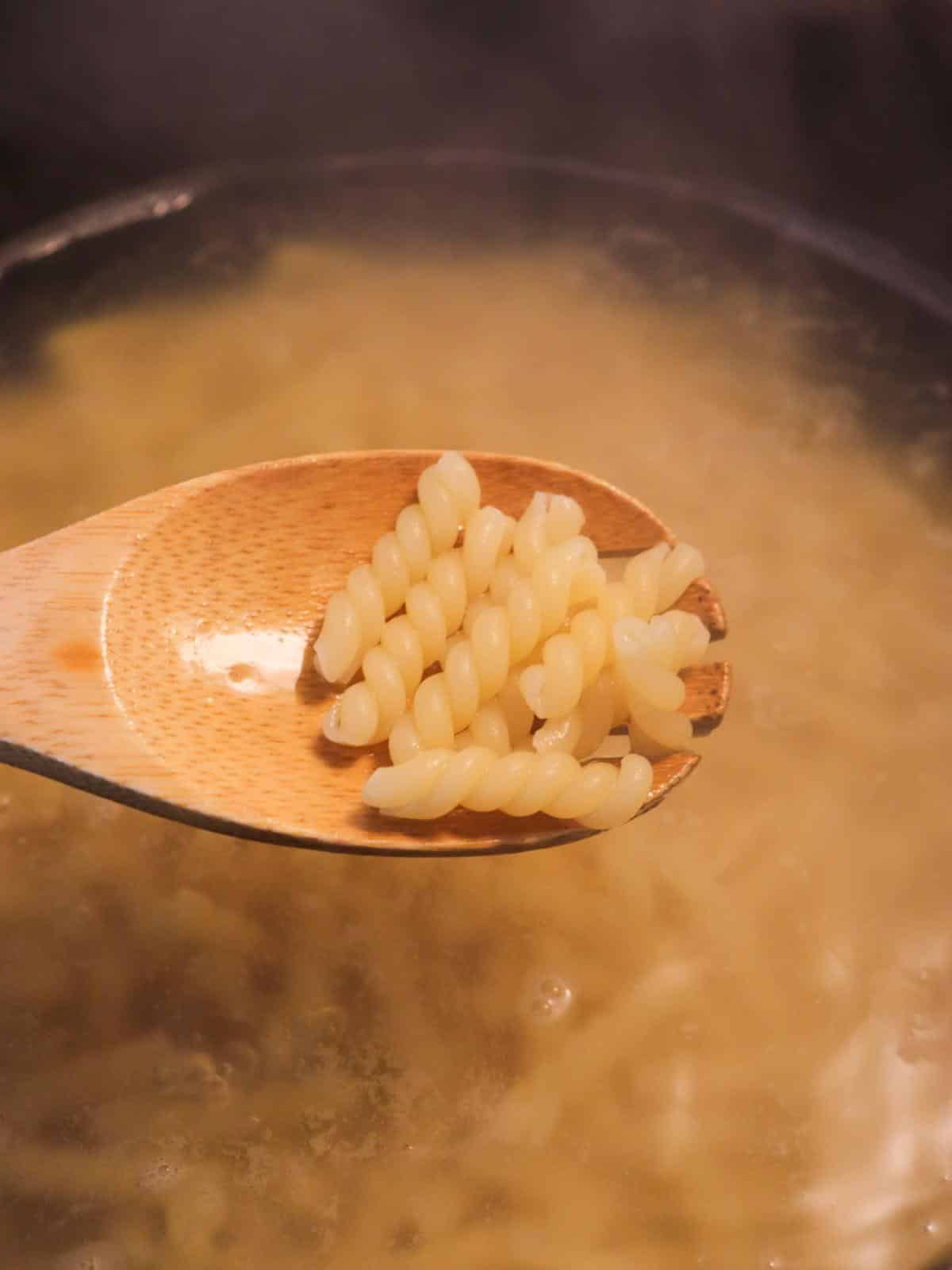 Wooden spoon stirring spiral pasta as it boils in a pan on a stove.