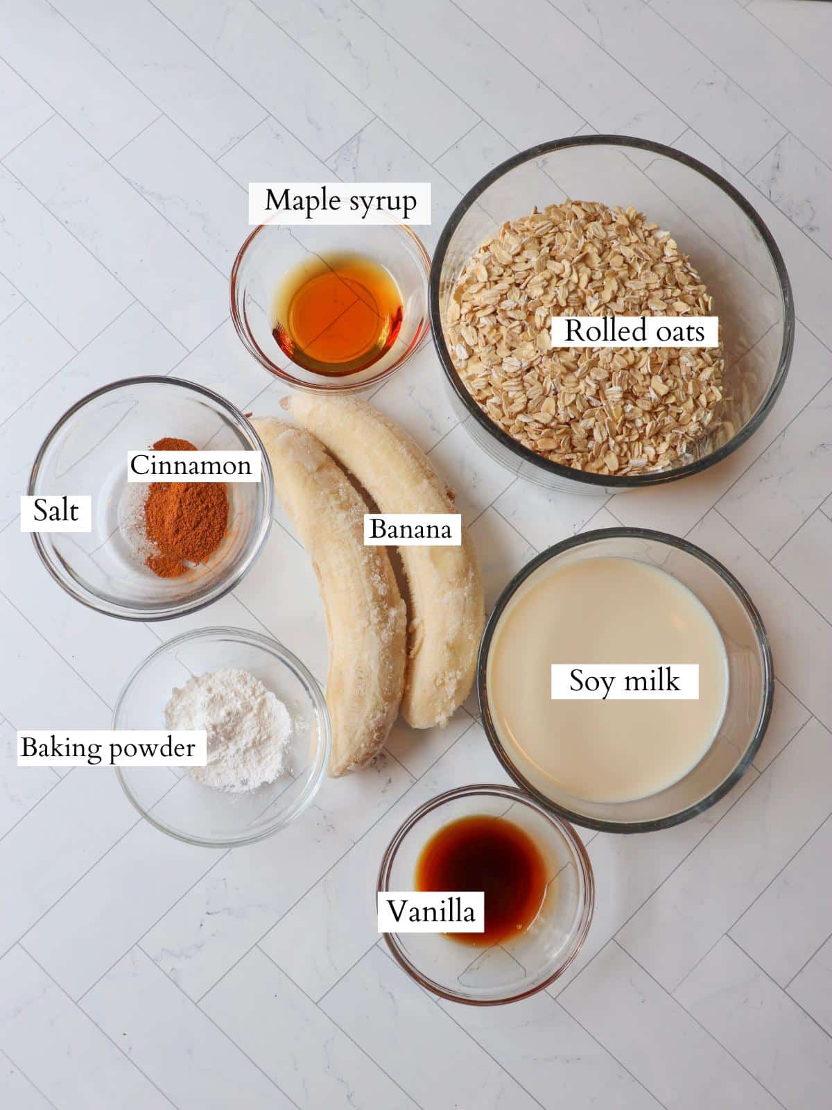Ingredients for vegan banana oatmeal pancakes laid out in small glass bowls on a kitchen counter.