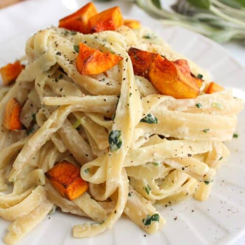 Creamy vegan fettuccini alfredo with roasted butternut squash and sage on a white plate.