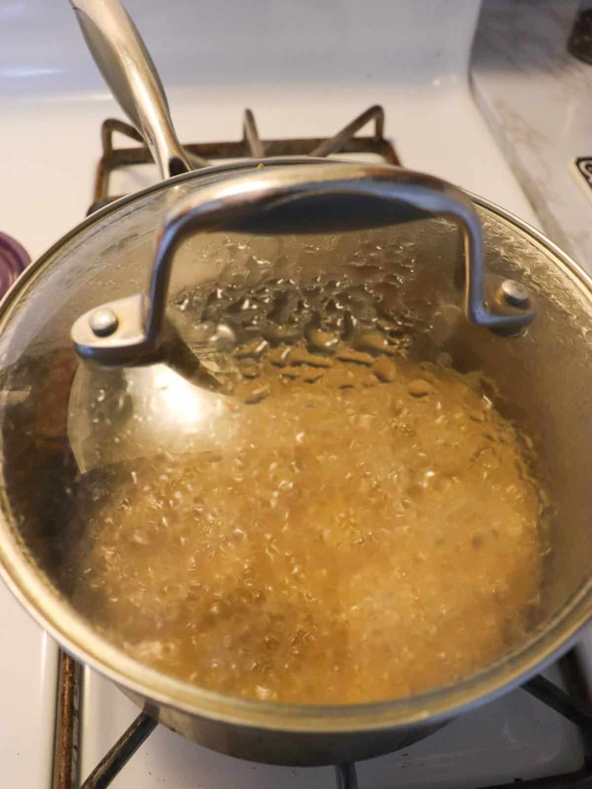 Quinoa cooking in a pan on a stove with the lid on.