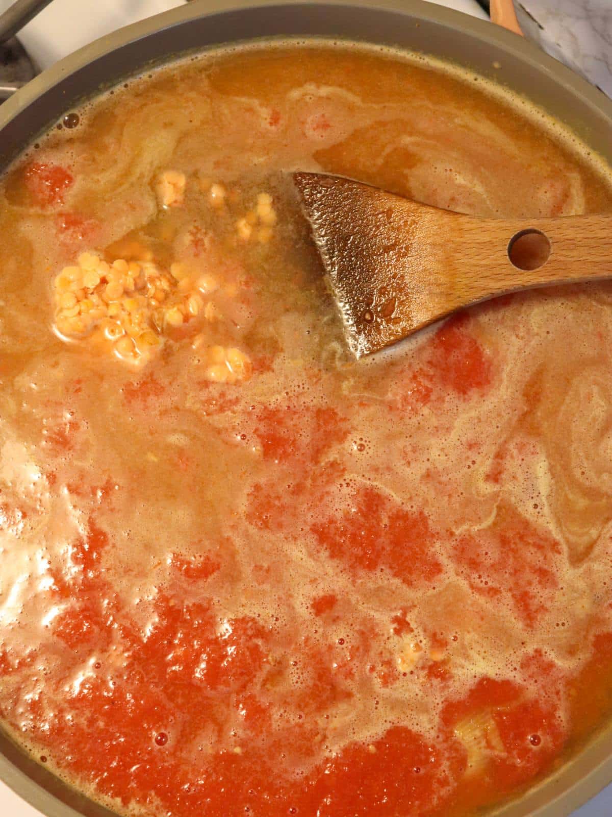 Red lentils, spices, crushed tomatoes and vegetable broth in a soup pan on the stove.