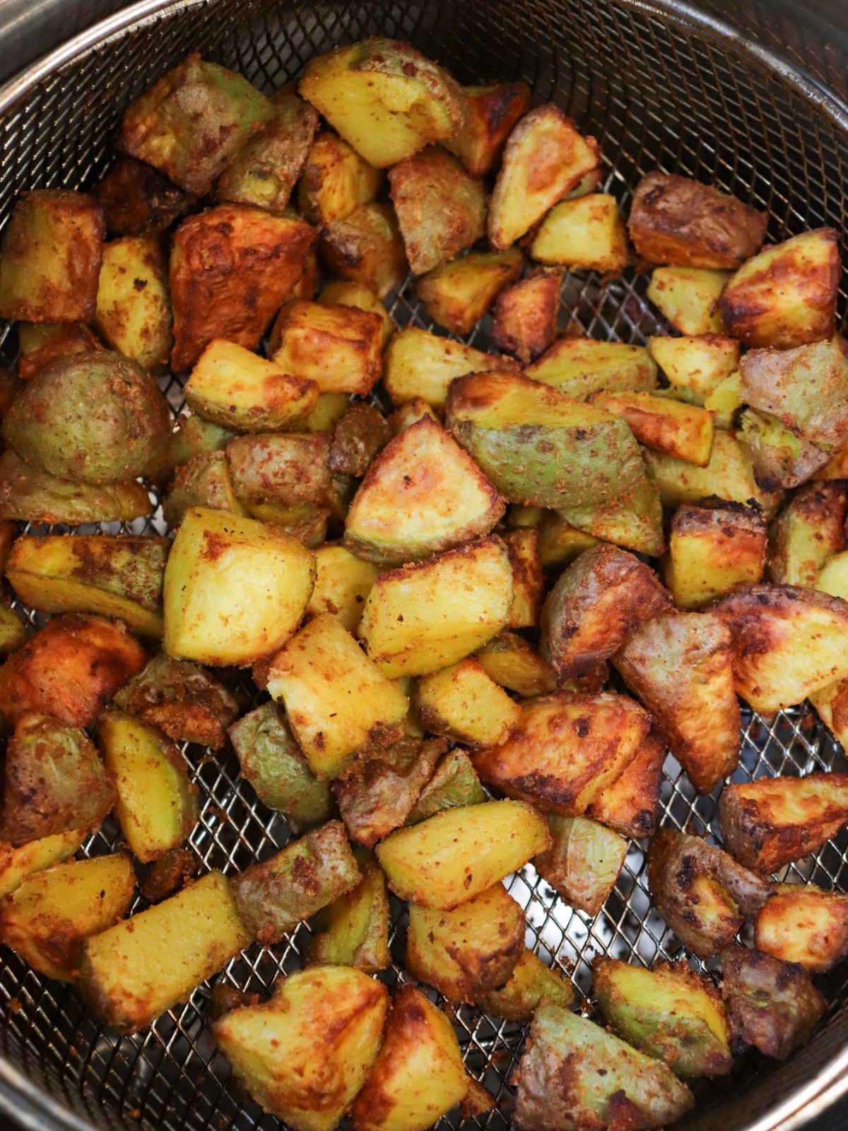 Air fried diced potatoes in an air fryer basket after being air fried.