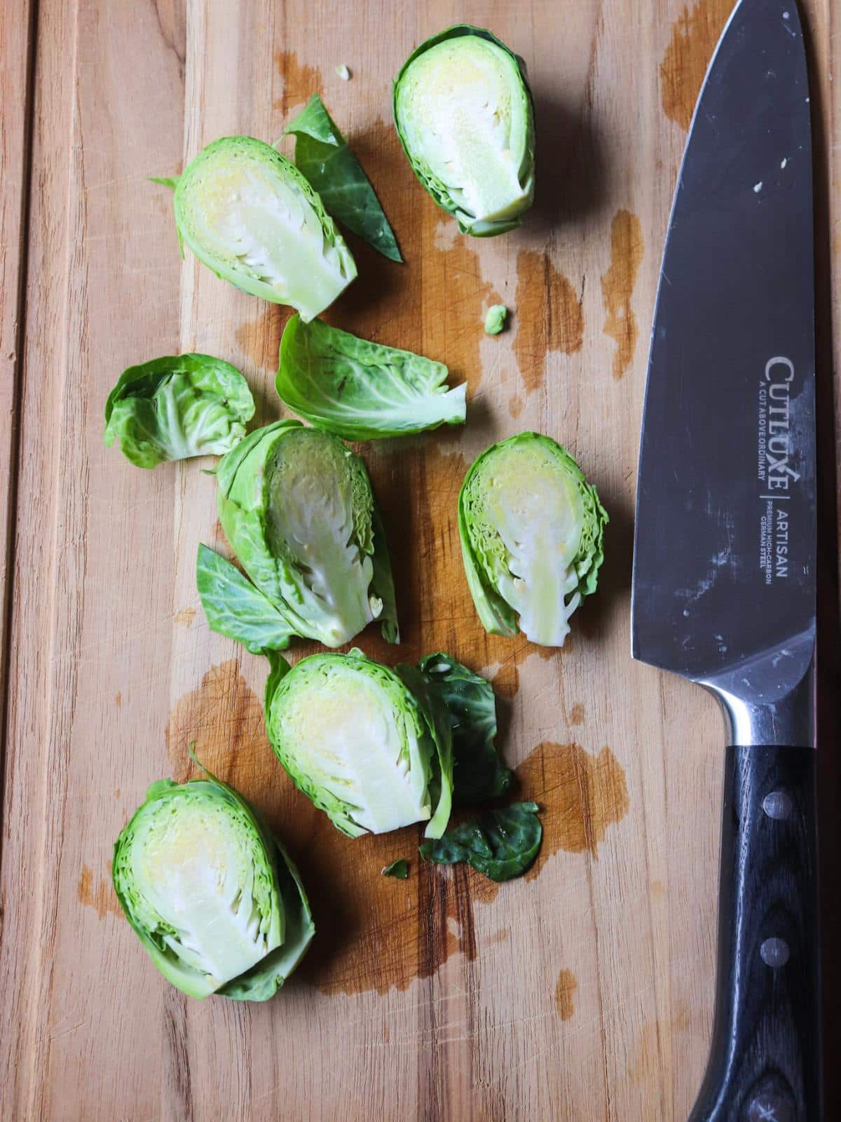 Brussels sprouts being cut in half on a wooden cutting board.