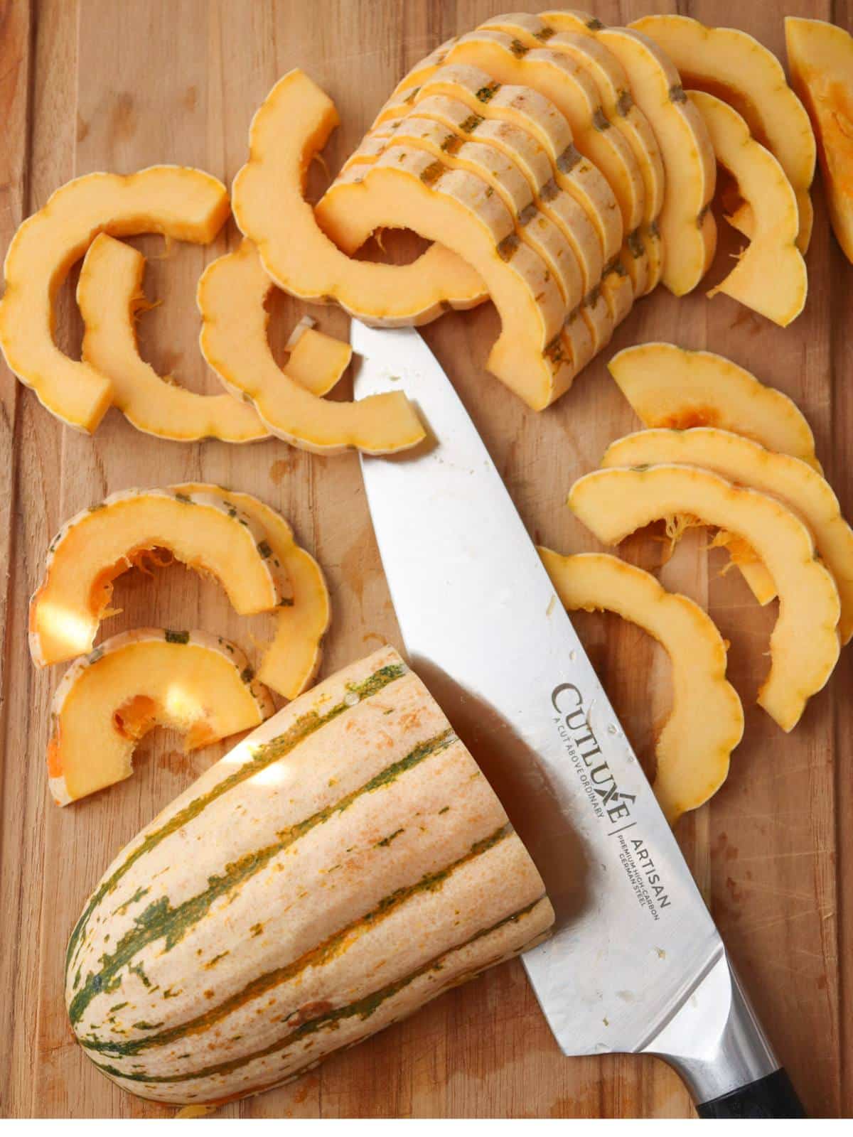 Delicata squash getting cut up on a wooden cutting board into strips.