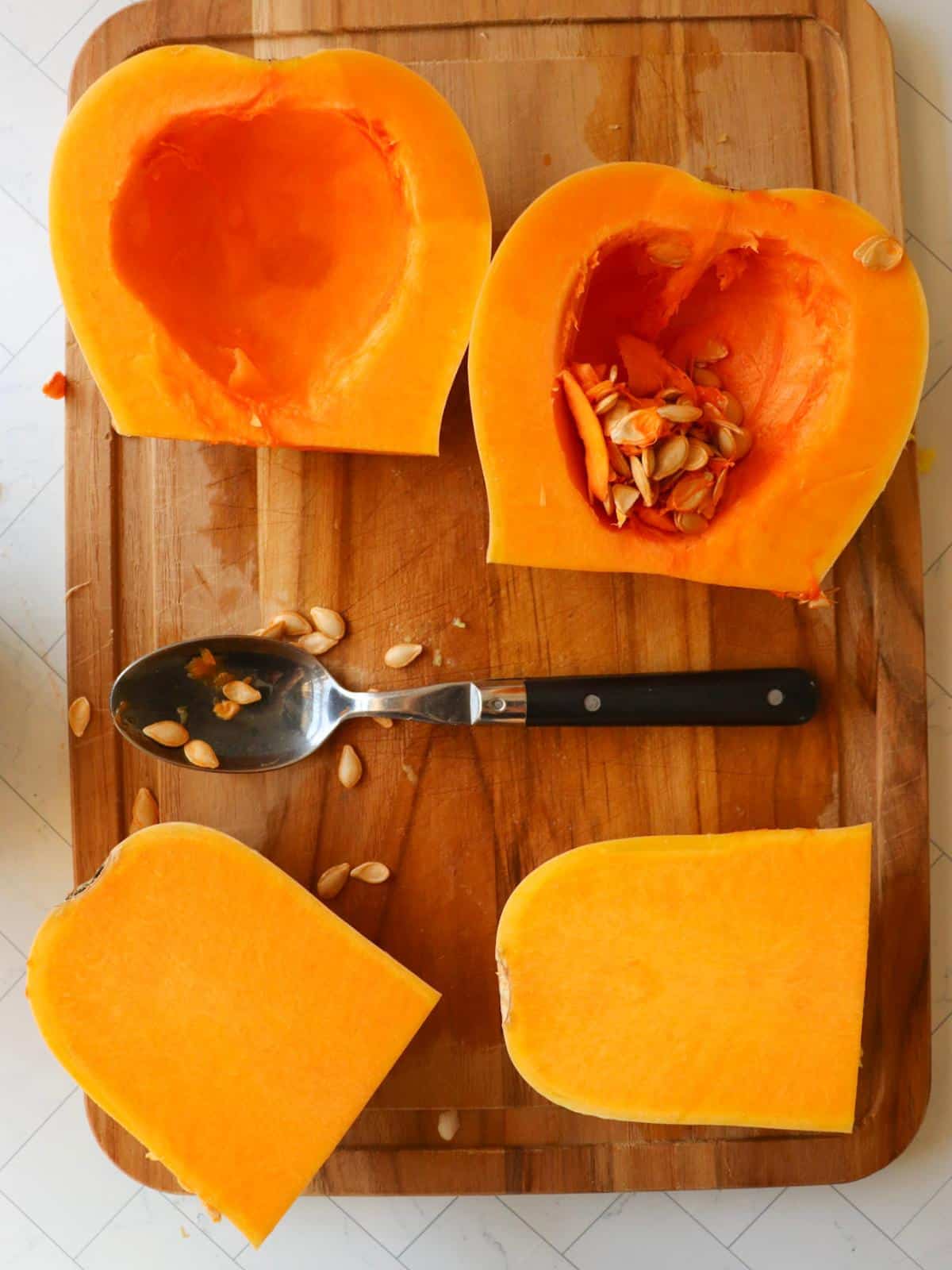 A butternut squash on a cutting board, with a spoon scooping out the inner seeds.