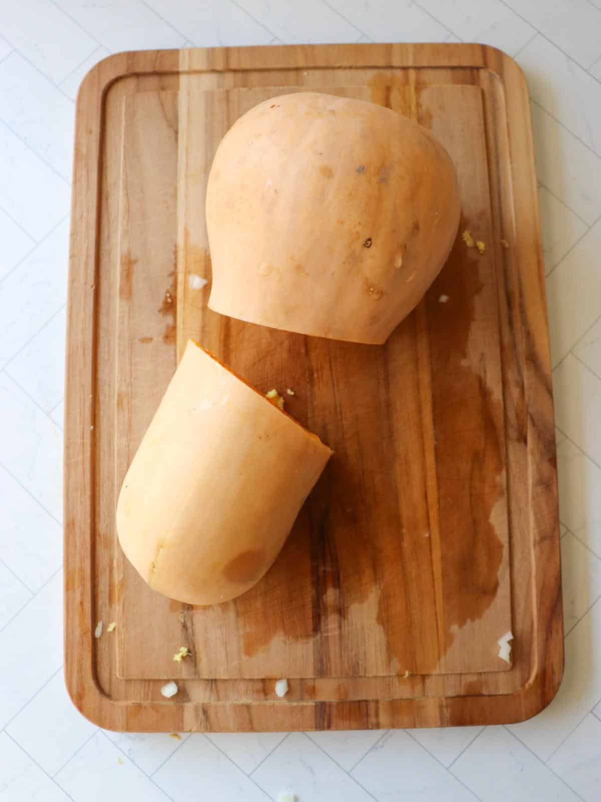 A butternut squash on a cutting board, cut in the middle.
