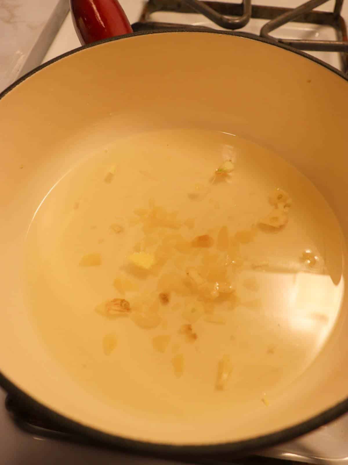 White wine and minced garlic in a fondue pot on the stove.