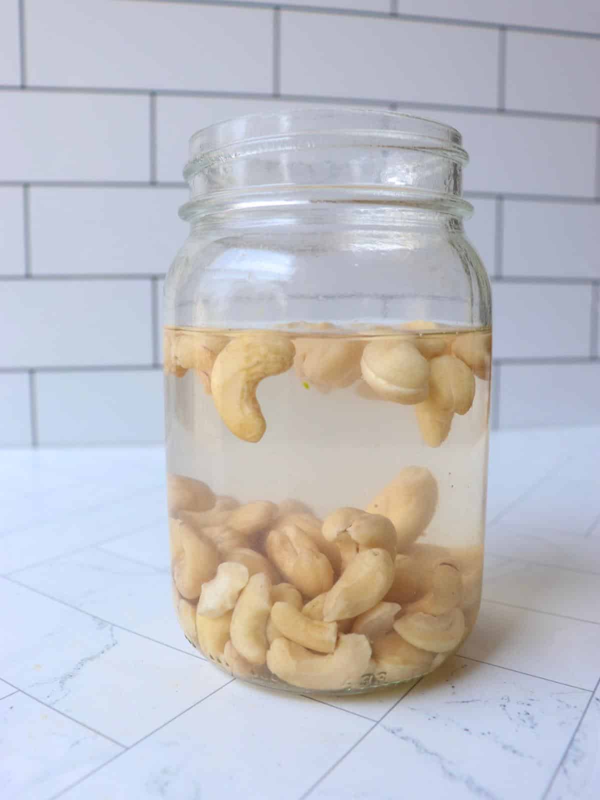 Raw cashews being soaked in boiled water in a mason jar.