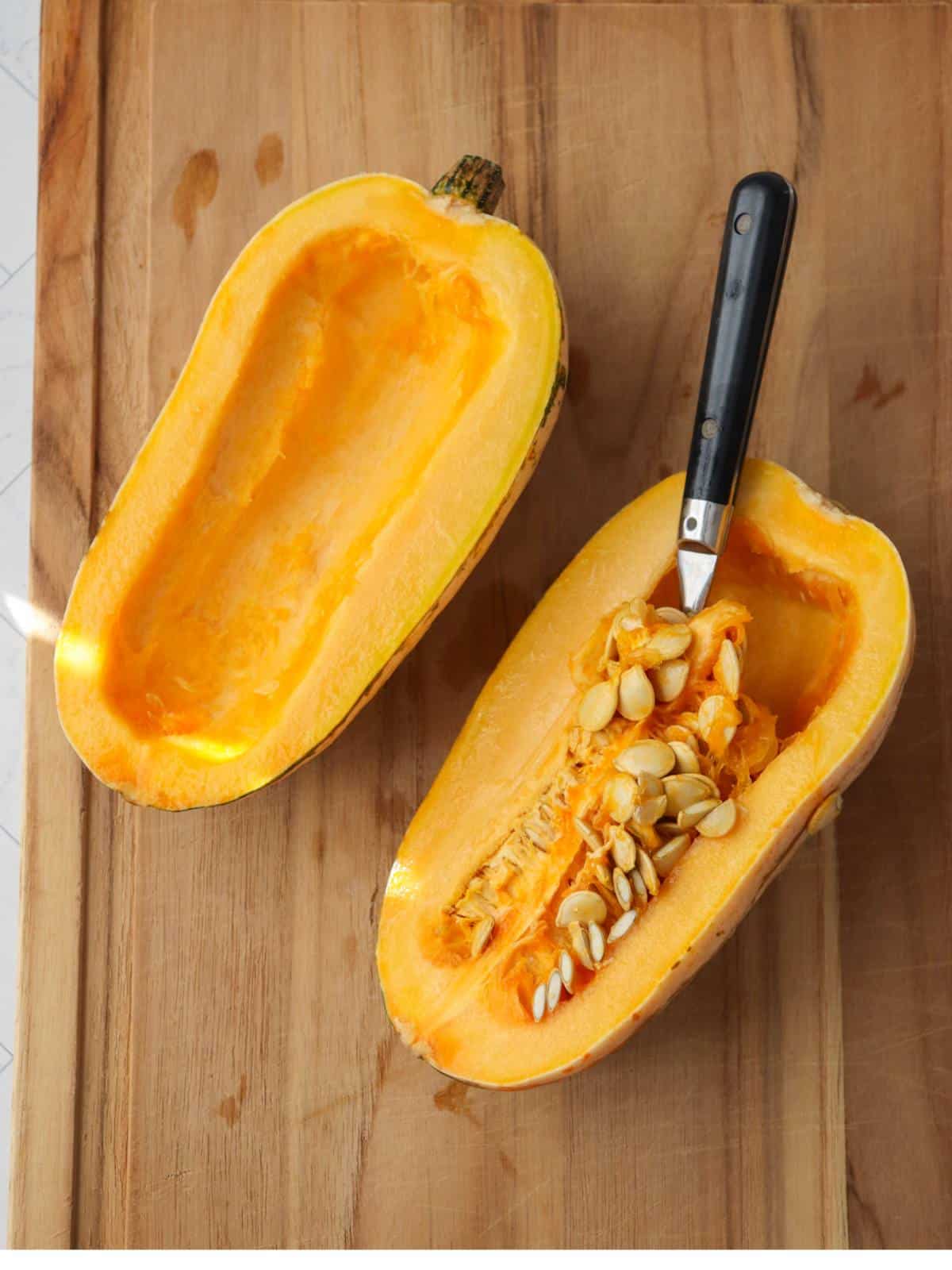Delicata squash cut in half on a cutting board with a spoon scooping out the seeds.