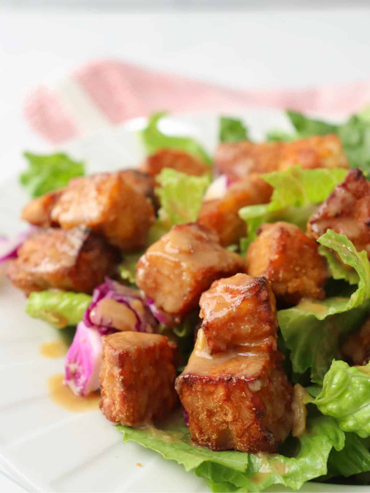 Air fryer tempeh cubes on top of a salad with a tahini dressing.