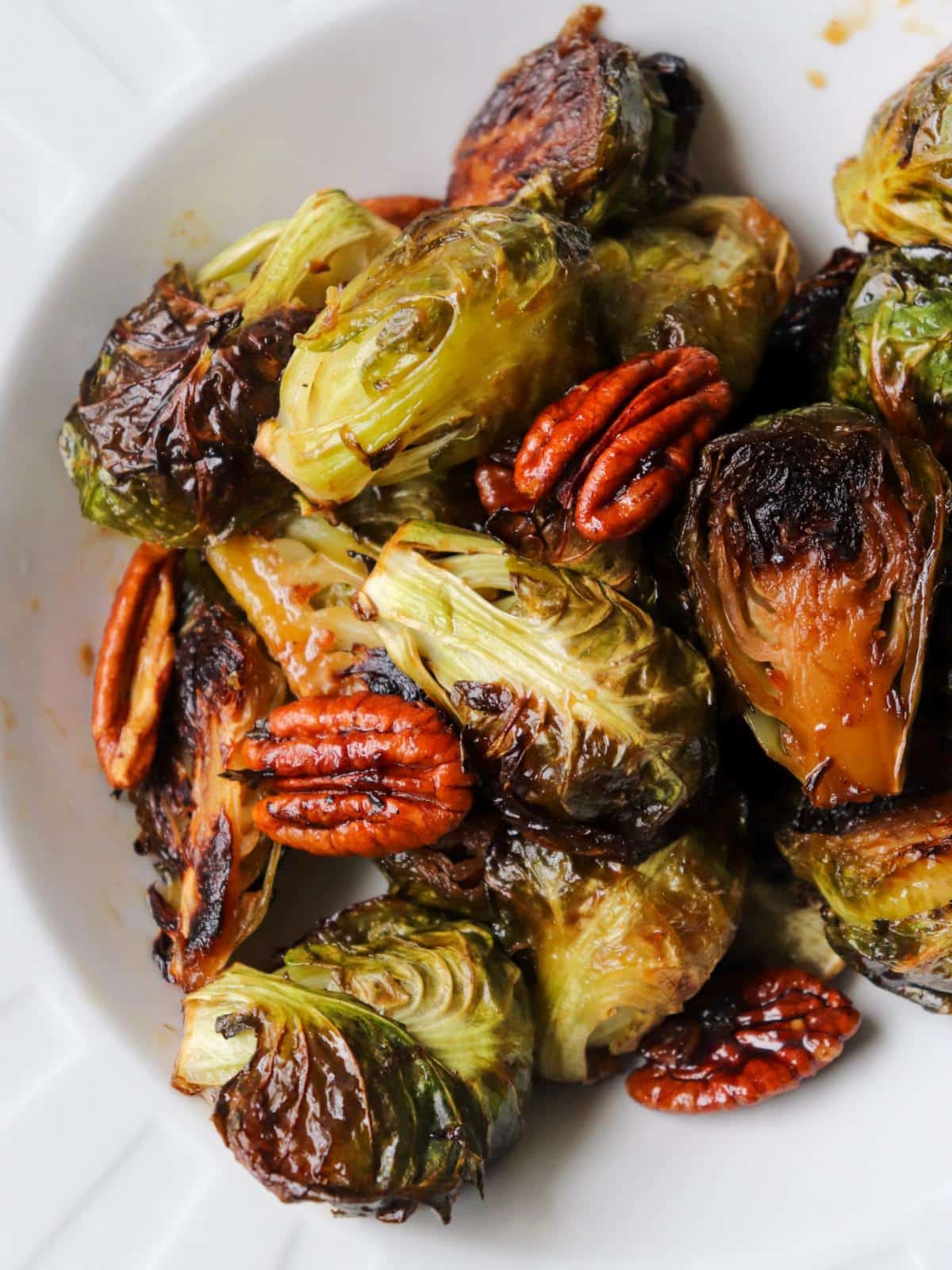 Candied brussel sprouts in a white bowl with pecans.