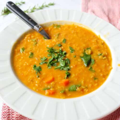 Creamy vegan red lentil coconut soup in a white soup bowl with a spoon and topped with fresh cilantro.