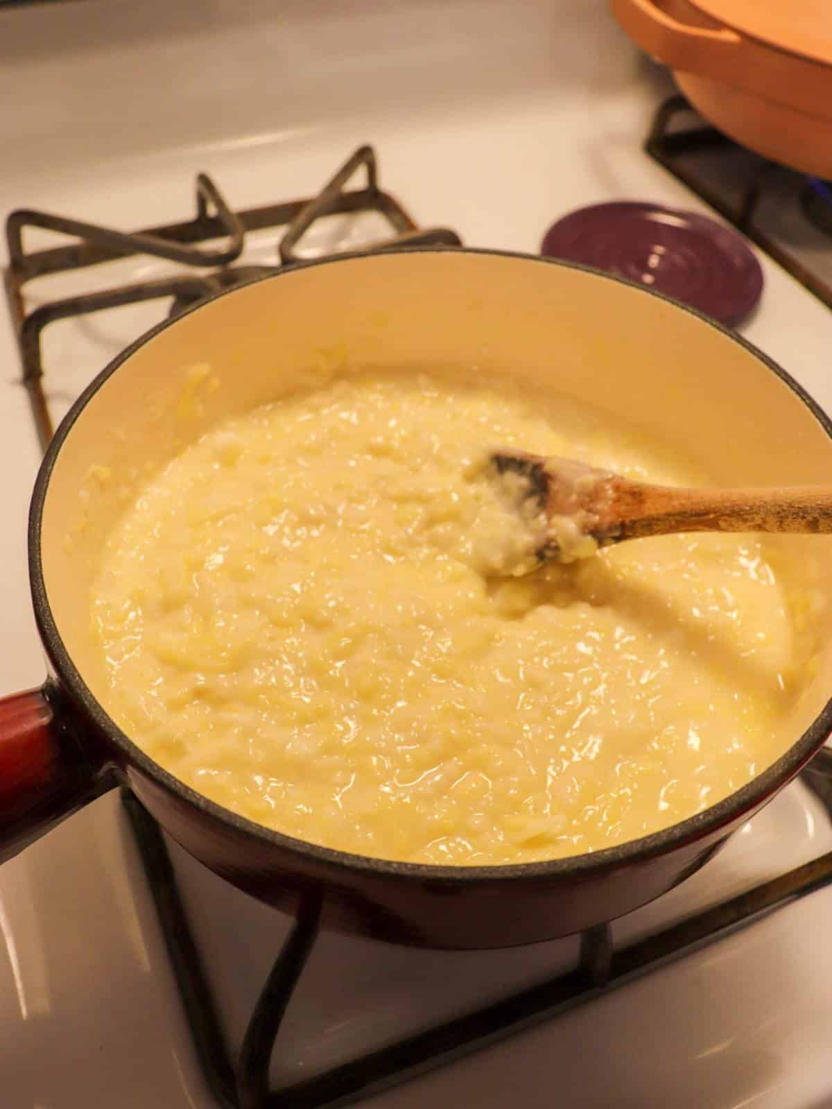 Vegan cheese melting in a fondue pot on the stove with a wooden spoon.