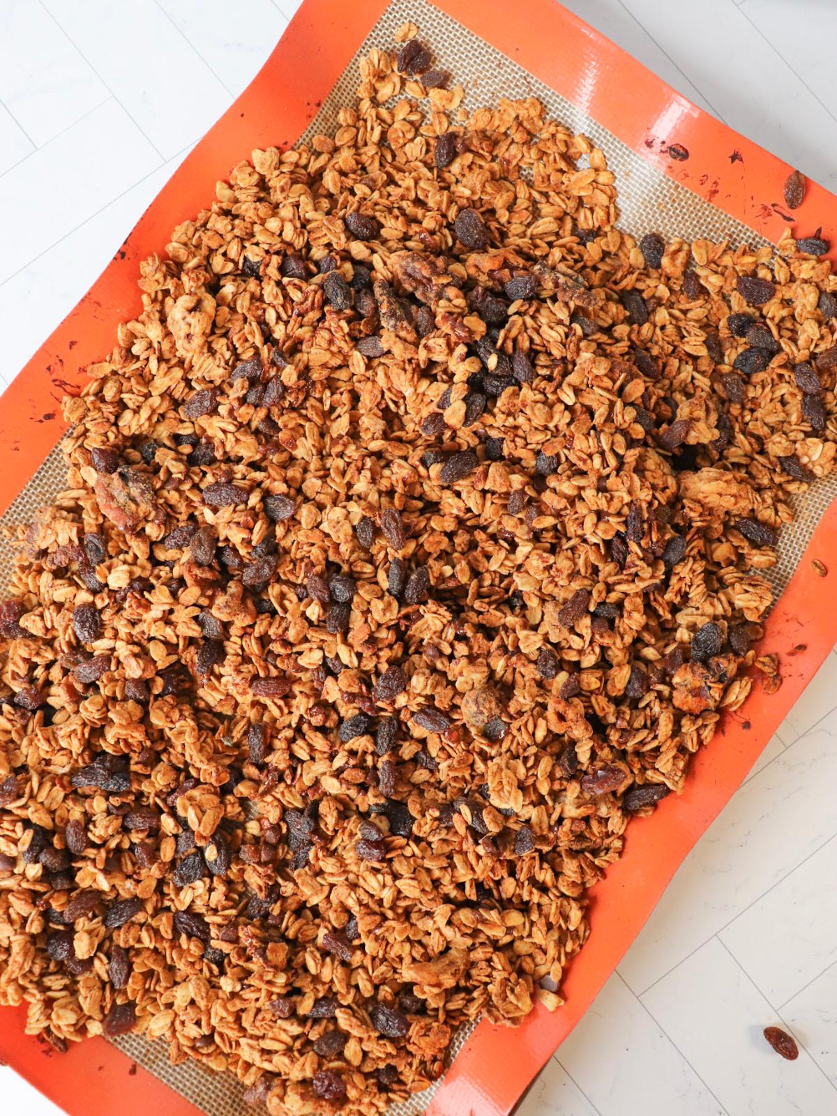 Vegan granola with raisins and chocolate chips on a baking sheet.
