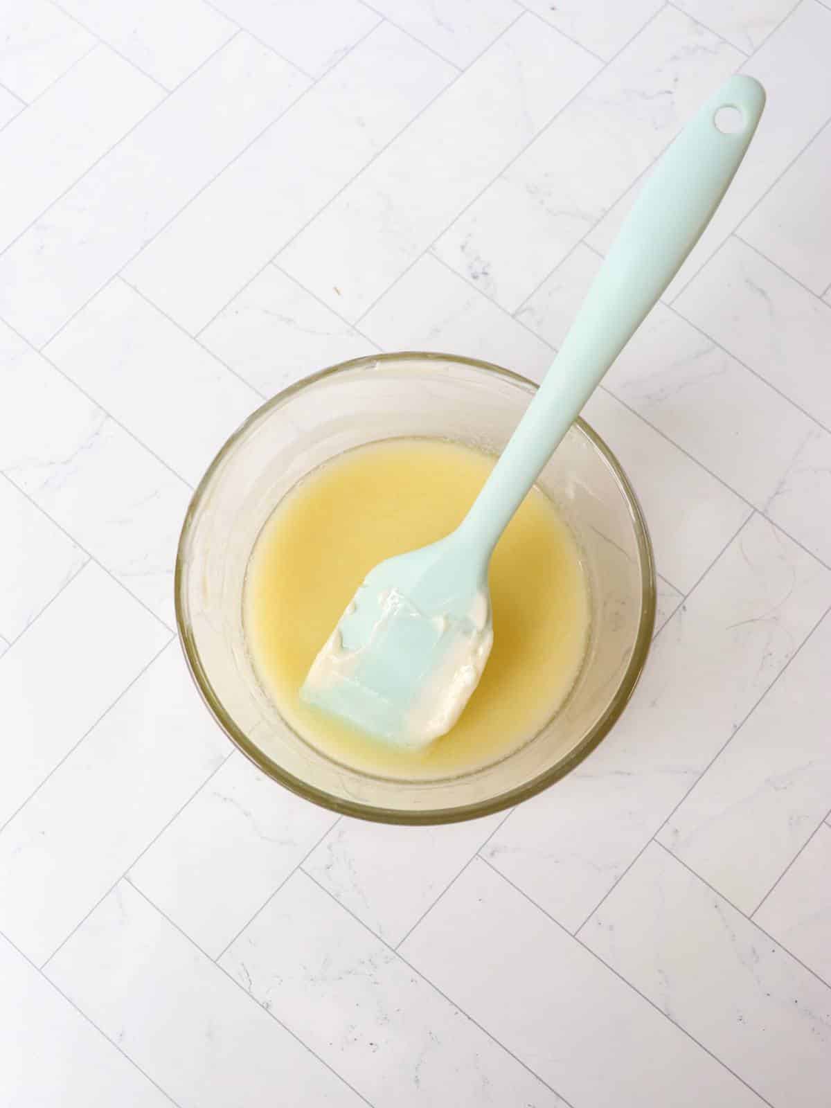 Melted vegan butter in a small glass bowl with a rubber spatula.
