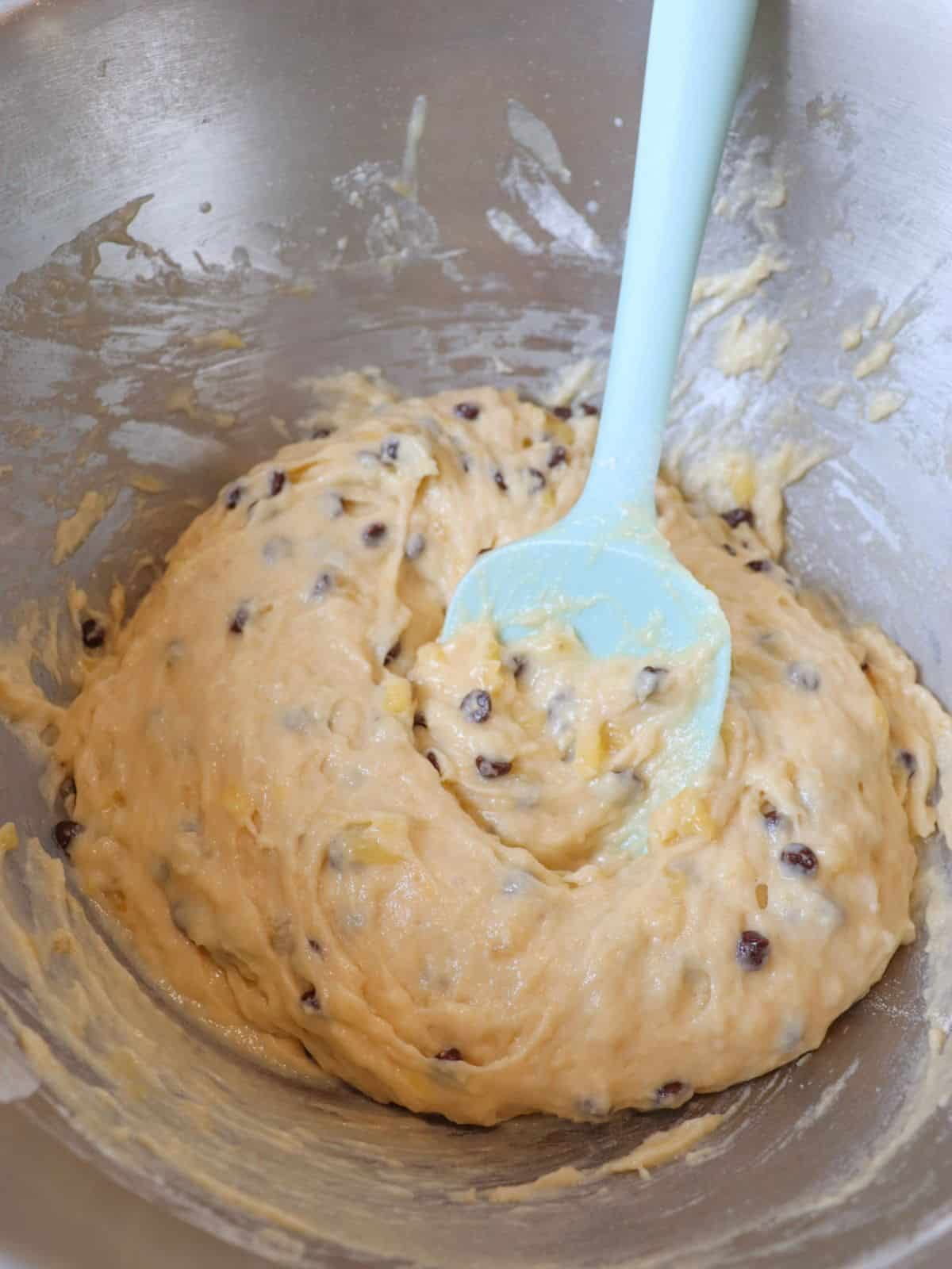 Vegan chocolate chip banana bread batter in a mixing bowl with a blue rubber spatula.