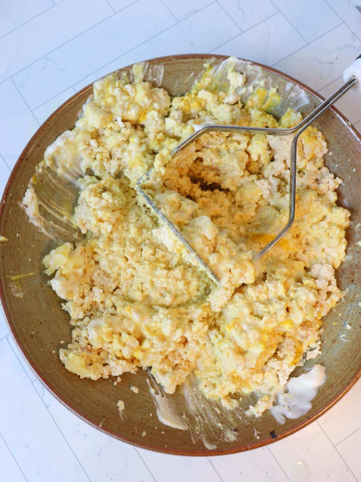 Vegan deviled egg filling in a mixing bowl with a potato masher.